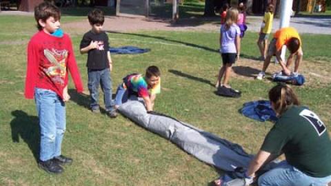 Youth rolling up tents after a camp-out with the help of their counselors.