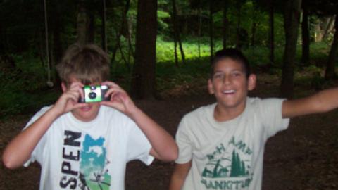 Two youth looking at camera. One is looking through camera at the camera.