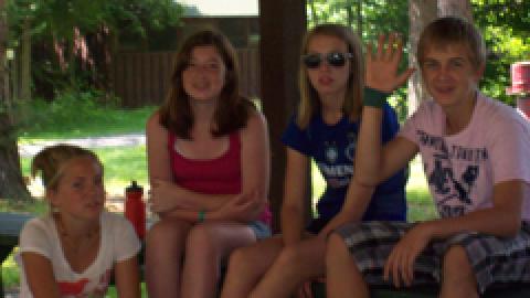 group of campers sitting together on a picnic table looking at the camera.