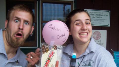 two counselors show off a recycled creation made of snack containers and a balloon.