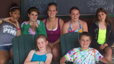 Six youth sit on stone bench with counselor in front of dining hall.