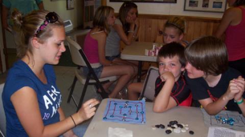 Campers sitting at table with counselor playing 9 mans morris.