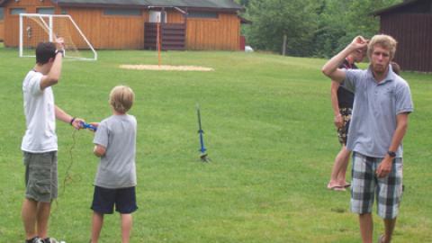 Counselor counting down while two campers prepare to launch model rockets.