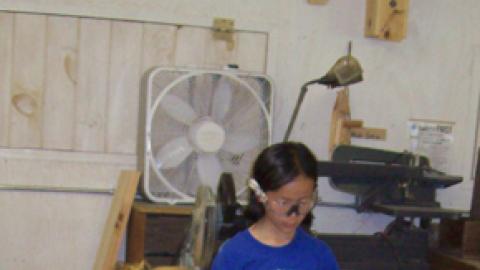 Counselor kneels down to assist camper with hack saw.