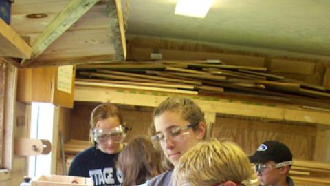 Counselors working one on one with campers at a scroll saw.