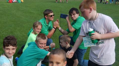 Youth shaking hands and kneeling in the grass. One youth standing to shake hands. 