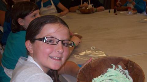 Youth smiling at camera holding bowl of green frosting.