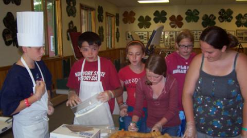 Campers wearing hair nets and aprons in front of pan of rolls.