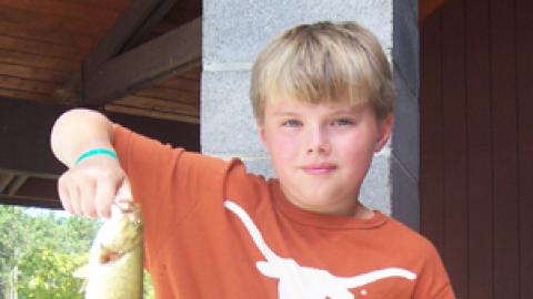Youth holding fish by mouth.