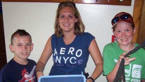 Two youth and staff holding bucket and net with fish they have just caught.