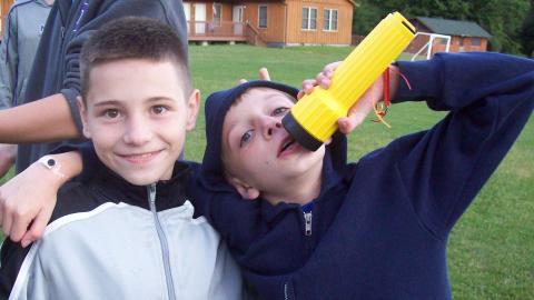 Youth with their arms around each other using a flashlight as a microphone. 