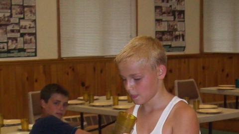 Camper setting the table. Another camper sits in the background watching. 