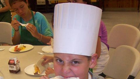 Camper wearing a chef's hat takes a bite out of a taco. 