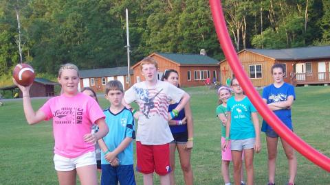 Youth standing in a line to throw a football through a hoop. 