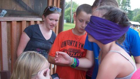 camper blind folded while putting make-up on another youth