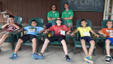 Youth relax in lawn chairs with their counselors standing in the background. 