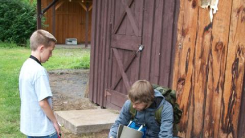 Counselor helps a youth strap his sleeping mat to a hiking backpack.