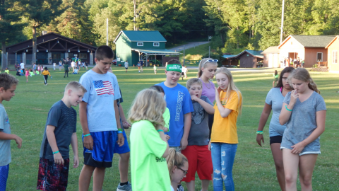 Campers standing around a seated counselor as they write on a paper.