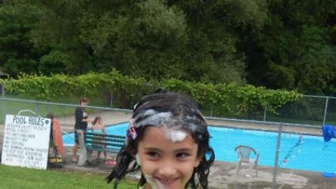 camper stands with bubbles in hair in front of the swimming pool