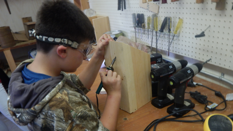camper using a tool to burn a design into their wooden butterfly house.
