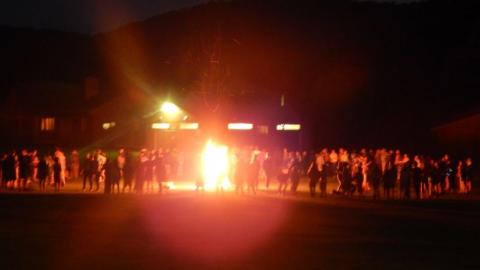 Campers stand outside a campfire at nighttime. 