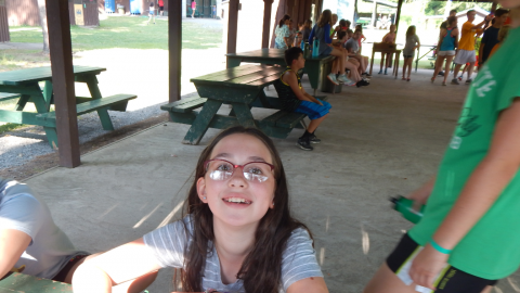 seated camper looks up from a "Shankitunk Challenge" paper smiling in Rec hall.
