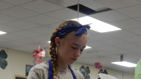 Youth wearing apron stands over a bowl of  ingredients stirring.