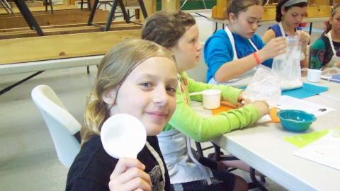 Youth participating in the chef's club holds up a measuring cup. 