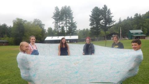 5 youth leaning back in a lyrca fabric tube to balance each other as counselor watches from outside the tube.