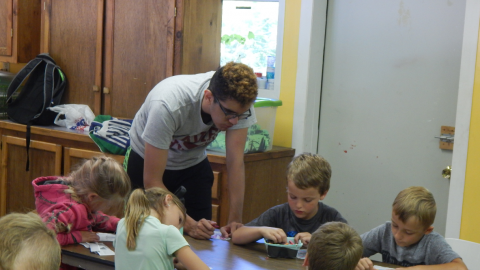 counselor leaning over a table of day campers who are writing.