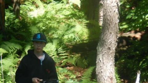 Campers fishing. One standing with pole in the water and one sitting on the bank putting bait on the hook.