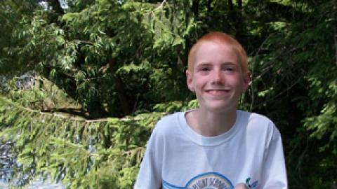 Smiling camper holds his fishing pole with a large fish dangling from the hook.