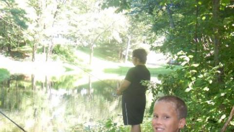 Camper smiling while fishing with another camper. 