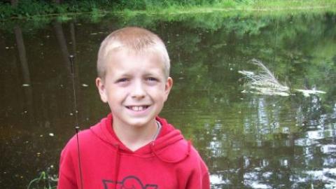 Youth stands with a fishing pole near the water. 
