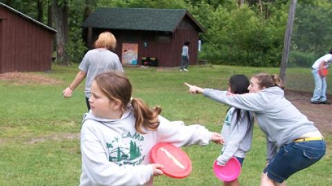 Youth engaged in a game of frisbee with a counselor whispering something to one of the youth holding a frisbee.