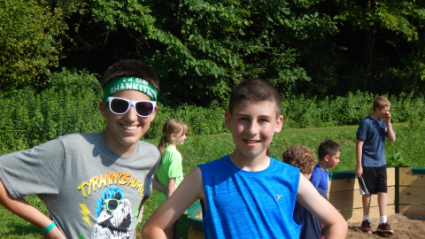 Two youth stand smiling near the gaga pit while others in the background are playing.