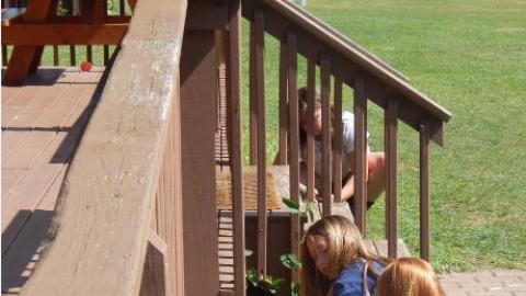 Youth search for objects under a porch while geocaching. 