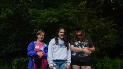 Three youth posing together for the camera in front of shrubbery.