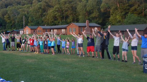 Large group of campers and staff in a line with hands raised and yelling/singing