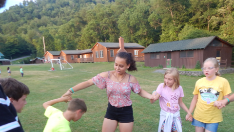 Youth in a circle holding hands and stepping through a hula hoop individually.