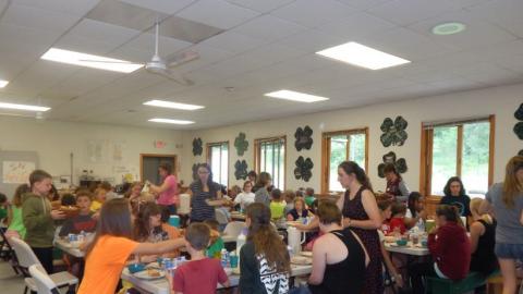 Youth sitting at tables in the dining hall and eating a meal. 