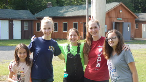 small group gathered together smiling near the flagpole. One youth is giving another bunny ears.