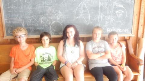 Youth sitting on a bench in front of the chalkboard. 