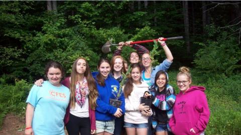 Youth smiling and holding trees to be planted outside. 