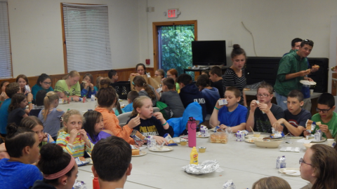 platoon groups seated around tables pushed together eating hotdogs after cook-out was rained out.