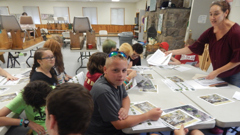 youth around the table looking at topographical maps with adult in front.