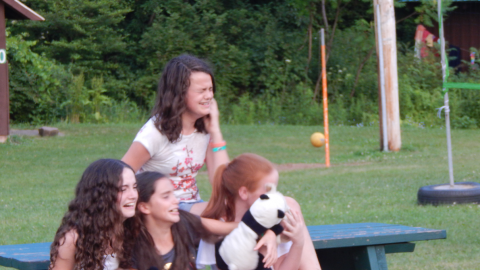 Cabin group seated on a picnic table pretending to laugh/cry hysterically while holding stuffed animals. 