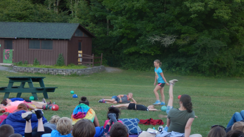 Standing youth over fellow cabinmates laying on ground with balls scattered between them.