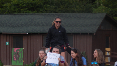 Cabin group sitting on a picnic table smiling. Counselor holds up a sign that reads "During rest."