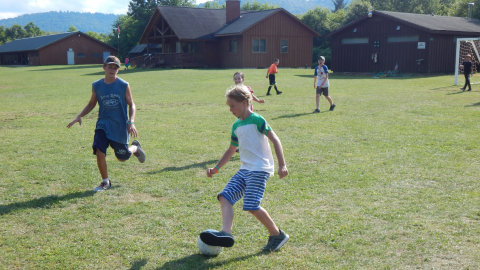 youth running down the soccer field one kicking the ball with the side of their foot.